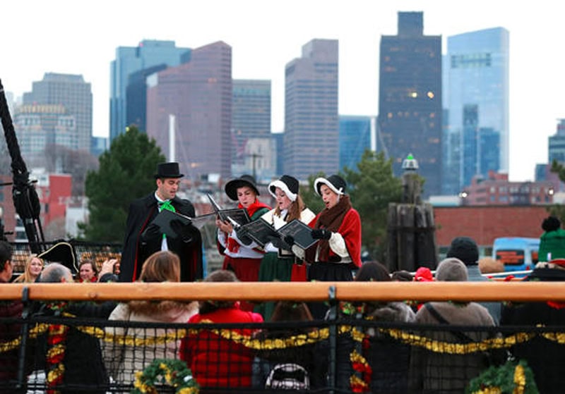 A far view of the carolers performing on "Old Ironsides," with Boston's skyline in the background.